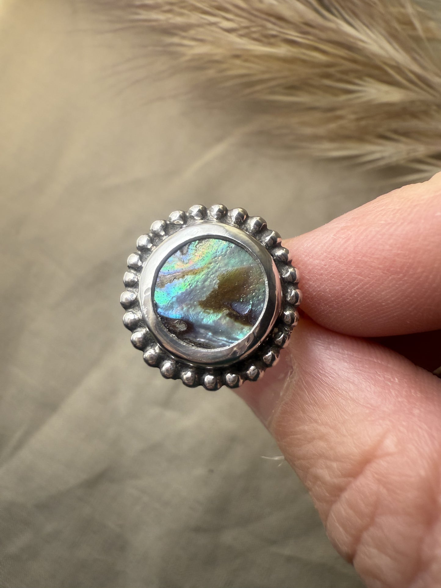 Close-up of iridescent abalone gemstone set in beaded sterling silver ring
